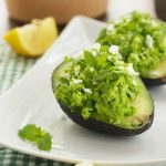 A close up of avocado boats on a square white plate and a green and white checked cloth.