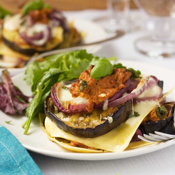 Freestyle eggplant lasagna on a white plate with another plate and glasses in the background