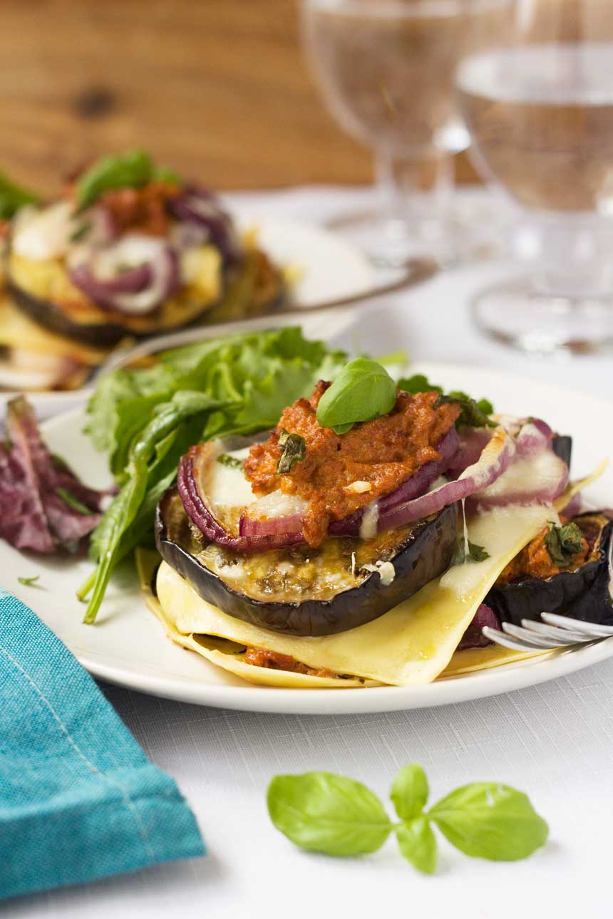 Freestyle eggplant lasagna on a white plate with another plate and glasses in the background