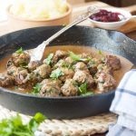A cast iron pan of Swedish meatballs with mashed potatoes and red sauce in the background