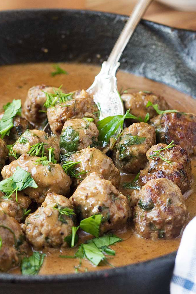 A close up of a cast iron pan of Swedish meatballs with a serving spoon in it
