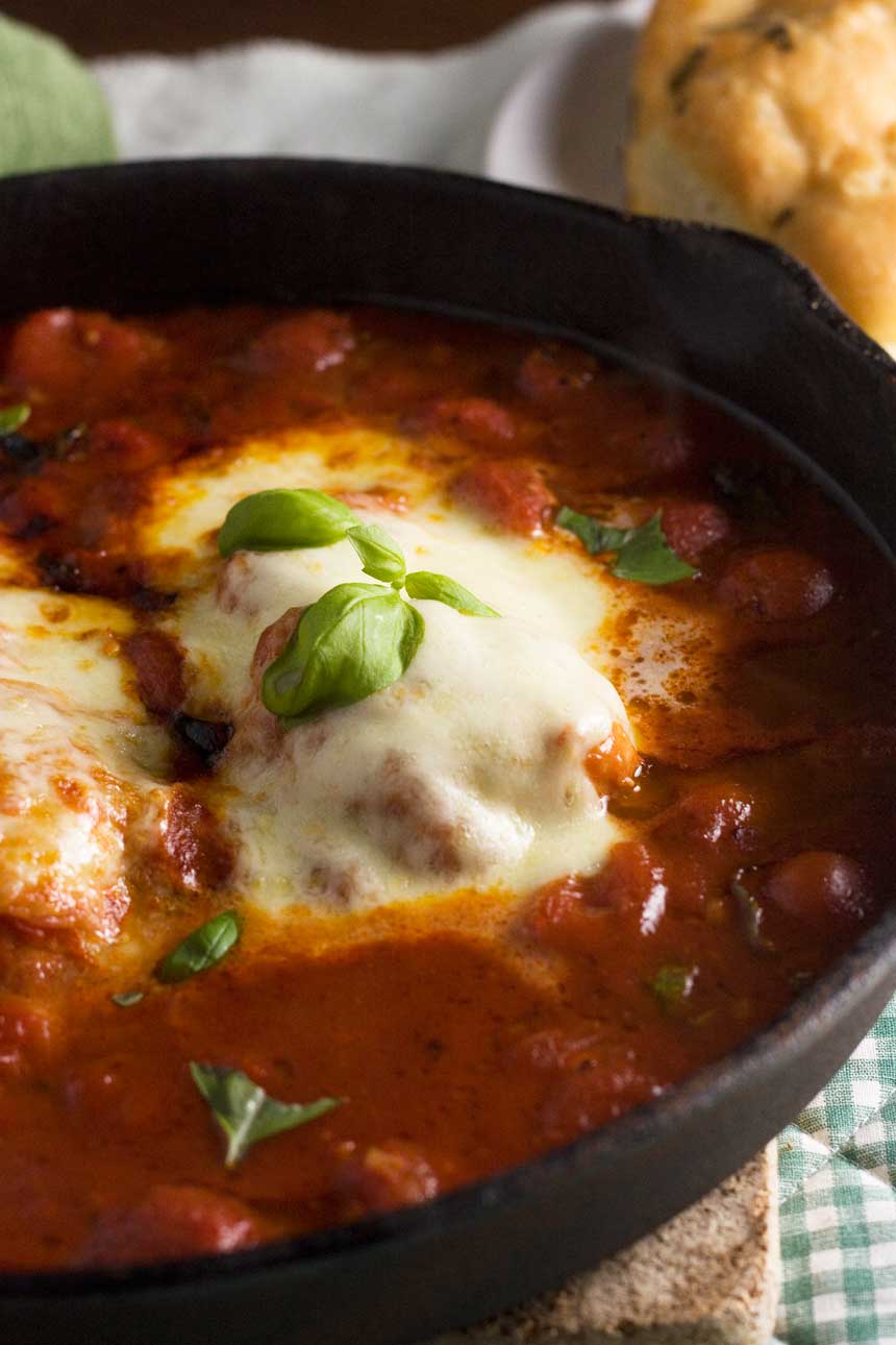 A close up of chicken with mozzarella and tomatoes in a cast iron pan