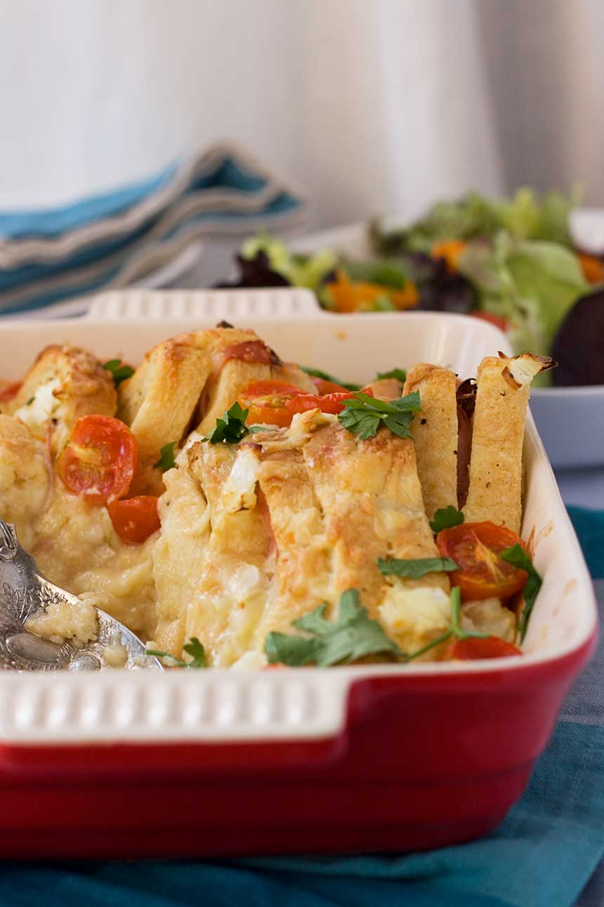 A closeup of the side of a baking dish of Croque monsieur brunch bake with salad and plates in the background.