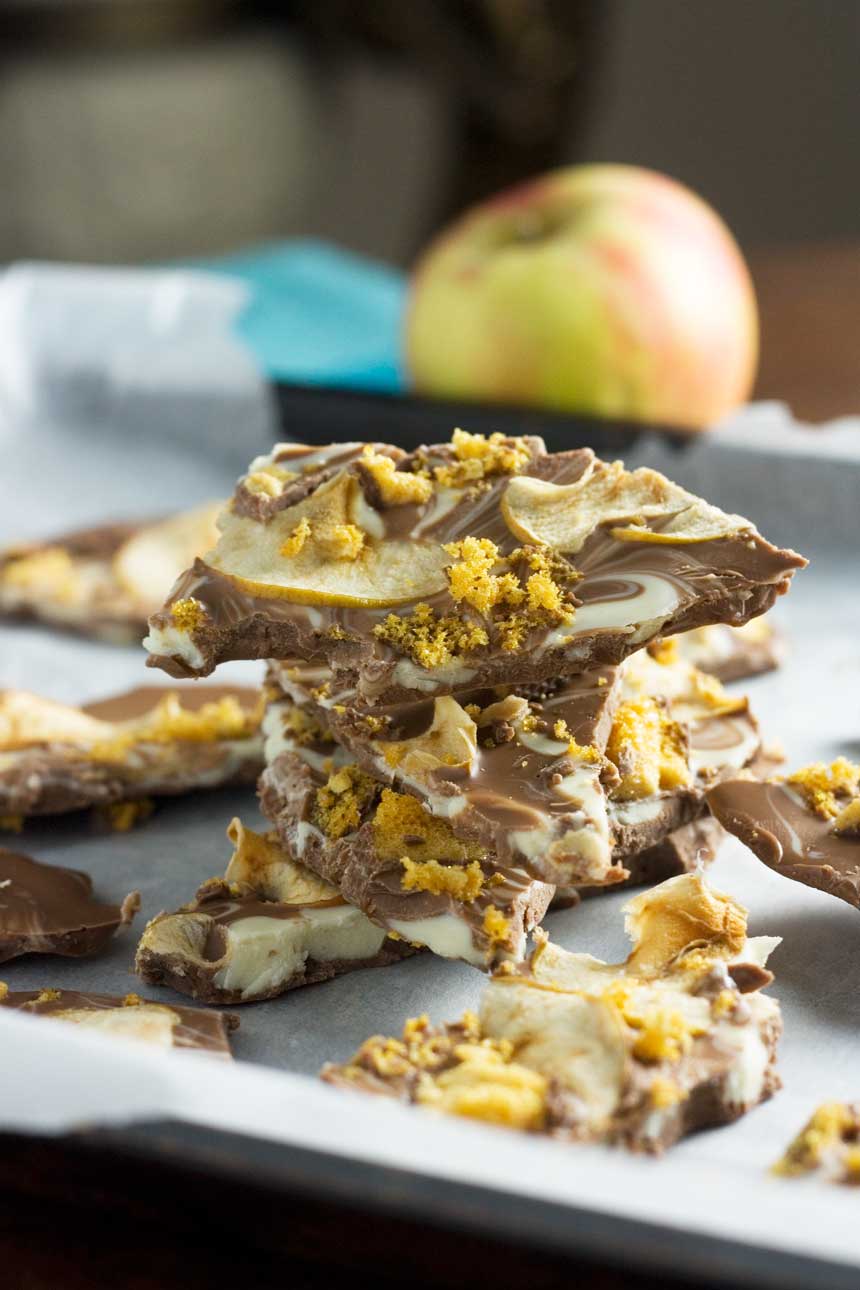 A closeup of a stack of toffee apple chocolate bark on baking paper with an apple in the background.