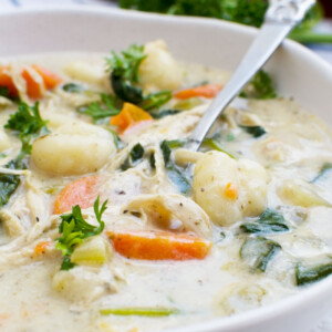 A close up of crockpot chicken gnocchi soup in a white bowl with a spoon
