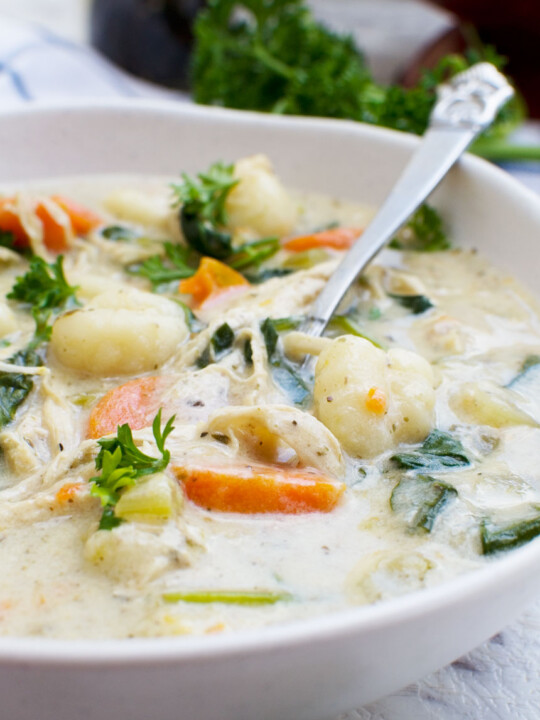 A close up of crockpot chicken gnocchi soup in a white bowl with a spoon