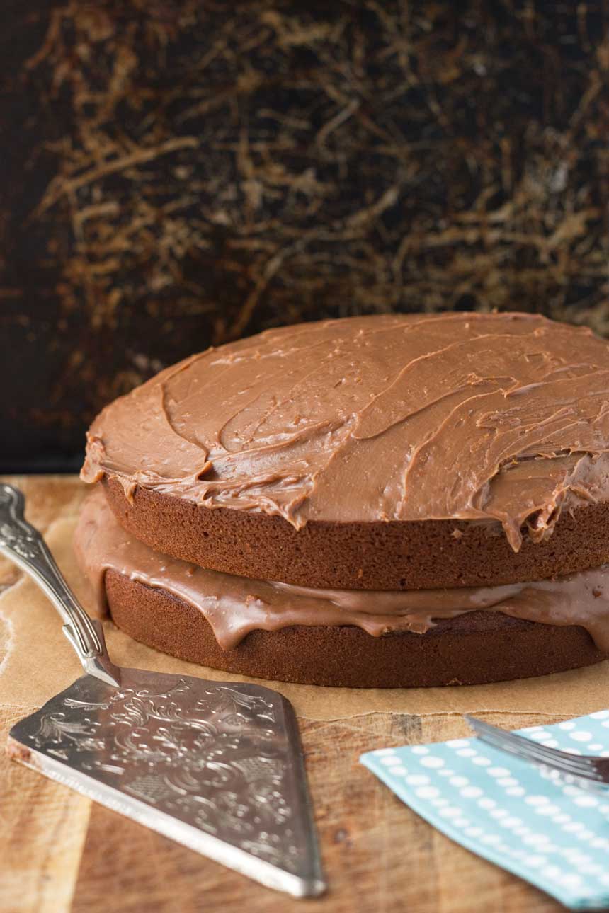 A whole chocolate orange cake on a wooden board with a decorative cake slice.