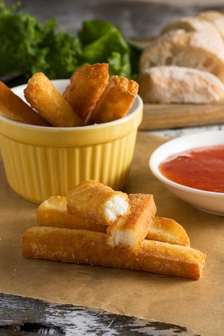 A small stack of crispy halloumi fries with more in a dish in the background