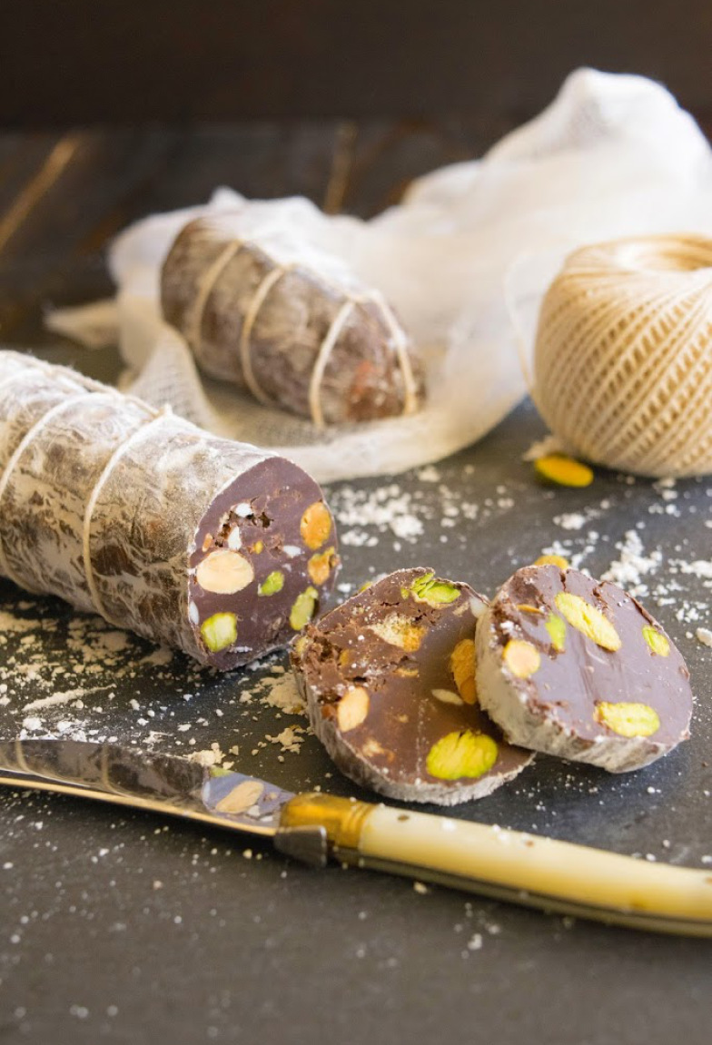 Chocolate salami by Culinary Ginger sliced on a black platter with a knife and some string.