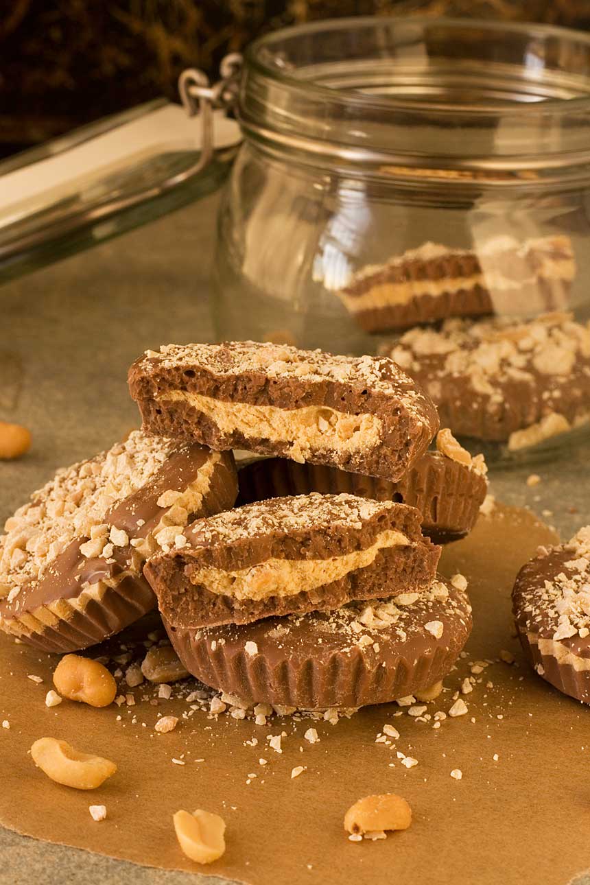 A pile of homemade peanut butter cups on a table with a jar behind.