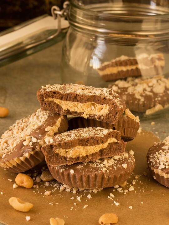 A pile of homemade peanut butter cups on a wooden table with a glass jar behind.