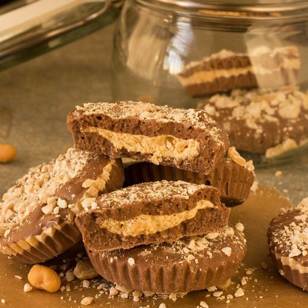 A pile of homemade peanut butter cups on a wooden table with a glass jar behind.