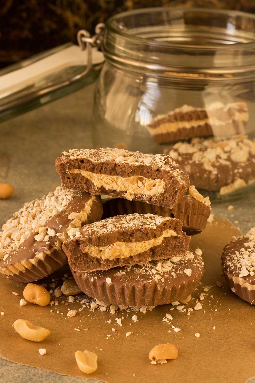 A pile of homemade peanut butter cups on a wooden table with a glass jar behind.