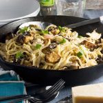 A black frying pan with turkey linguine in it and with kitchen equipment and ingredients around it.