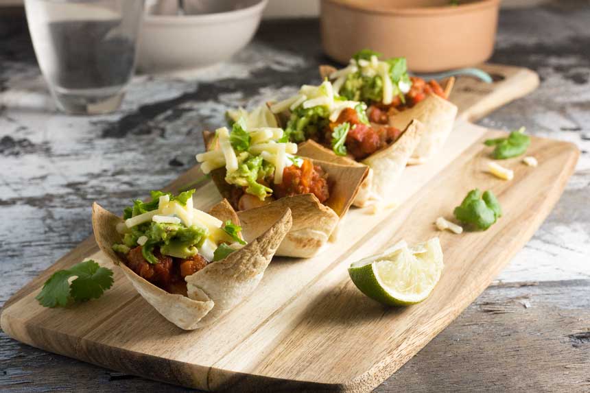 Turkey chili mini taco bowls in a row on a wooden board with lime wedges.