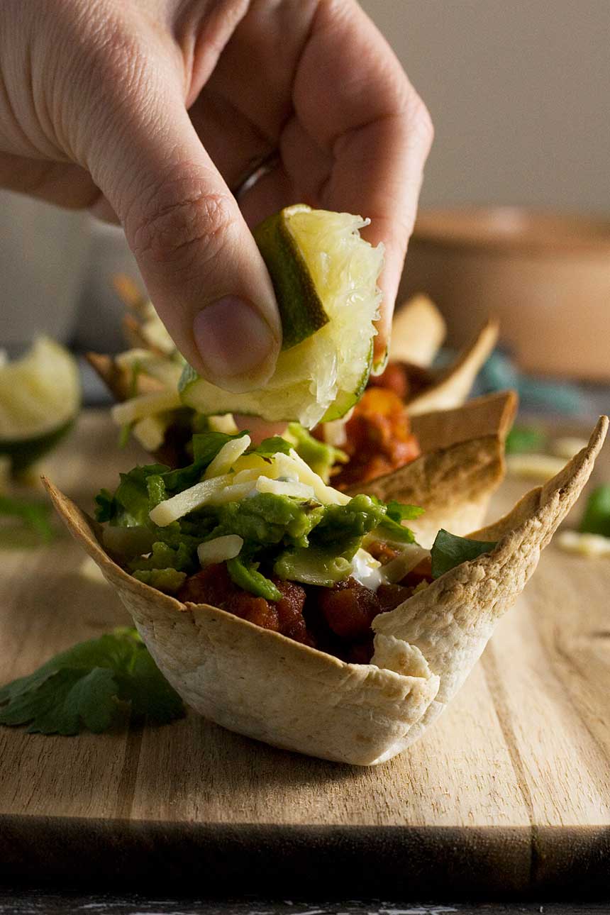 Someone squeezing lime over a turkey chili mini taco bowl on a wooden board.