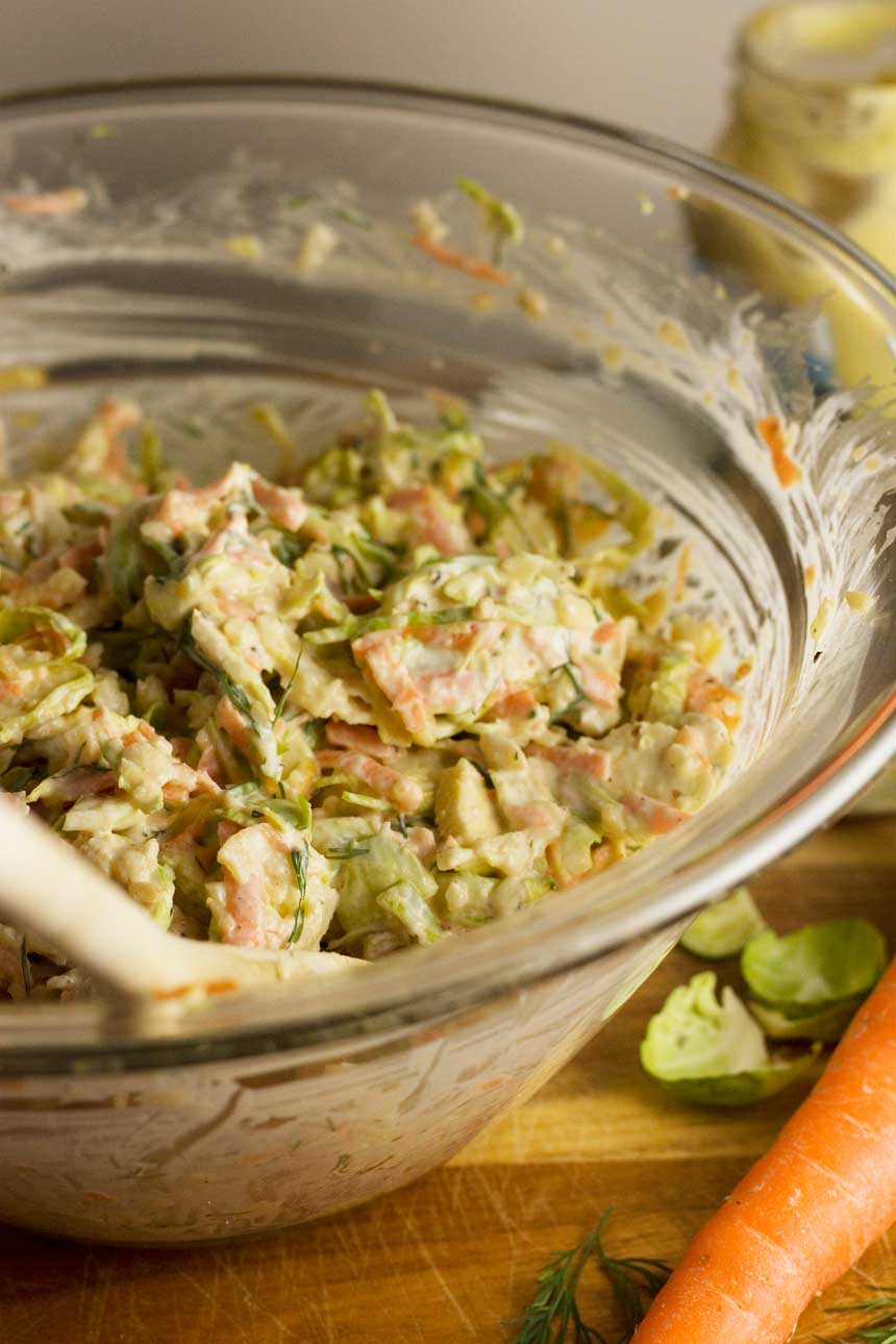 Clear bowl of Brussels sprouts coleslaw with a wooden spoon in it.