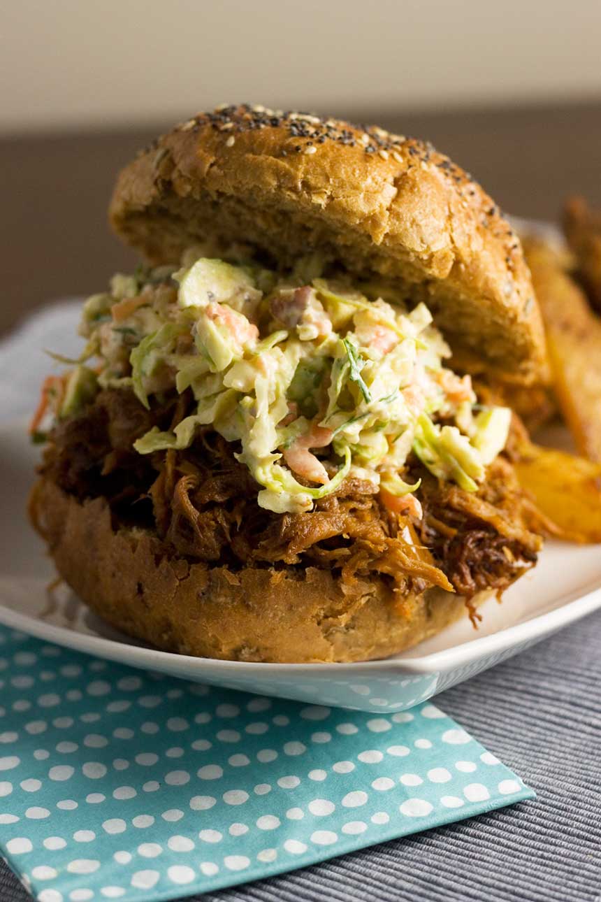 A close up of a pulled pork sandwich on a white plate with brussels sprouts coleslaw on it.