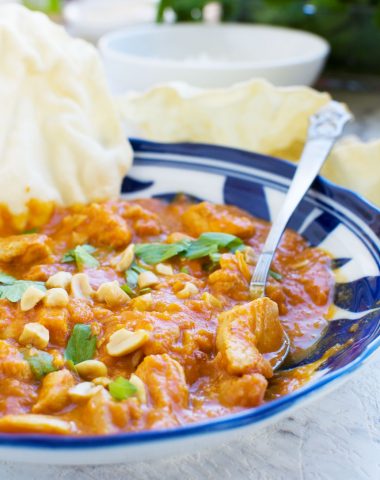A Thai chicken and butternut squash curry with peanuts, coriander & poppadoms, with a spoon in it