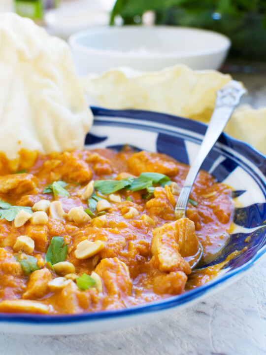 A Thai chicken and butternut squash curry with peanuts, coriander & poppadoms, with a spoon in it