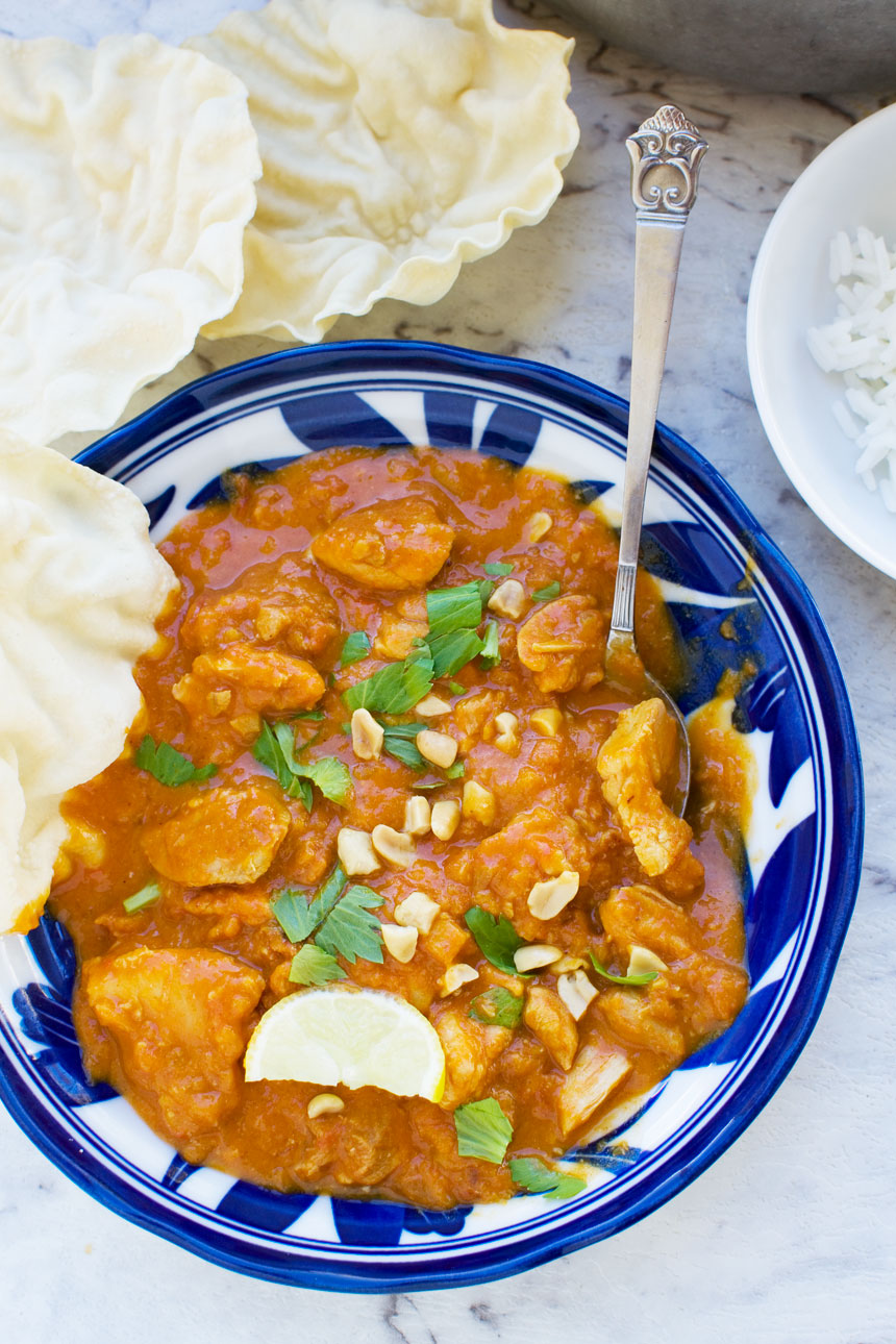 An overhead view of a Thai chicken and butternut squash curry with peanuts, coriander and poppadoms, with a spoon in it