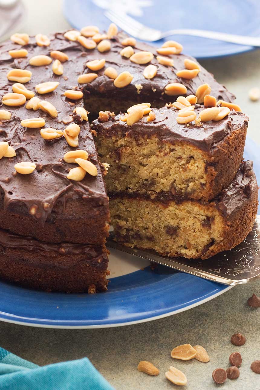 Closeup of a slice of peanut butter banana choc chip cake being taken out of a whole cake on a blue plate.