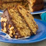 Slice of banana peanut butter cake on a blue plate with a fork and the rest of the cake in the background