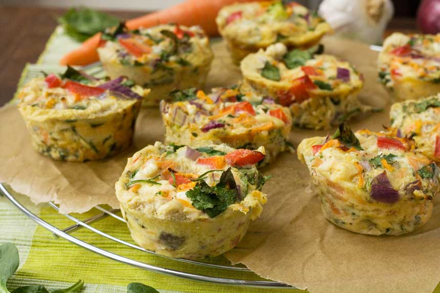 A closeup of veggie muffin frittatas on brown paper and a wire rack and on a green cloth.