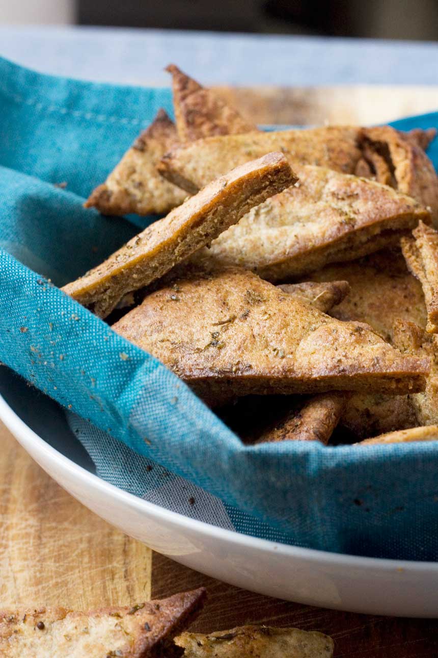 A big bowl of homemade Greek pita chips nestled inside a blue tea towel