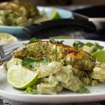 Jerk salmon and yogurt potatoes on a white plate with another plate of food in the background.