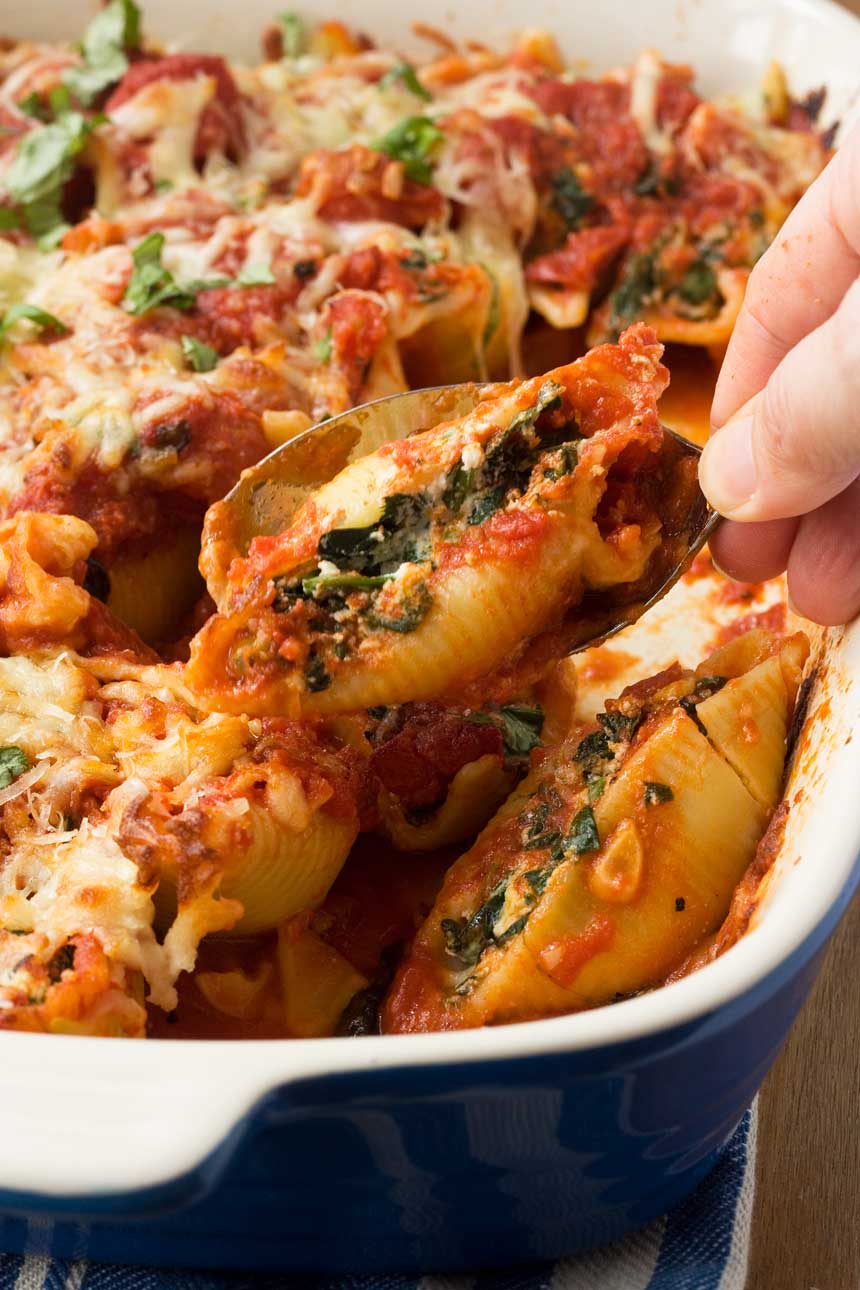 Someone spooning Baked spinach and ricotta shells out of a blue baking dish.