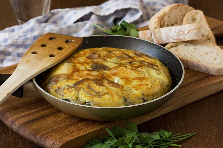 A whole Spanish omelette in an omelette pan with ingredients in the background