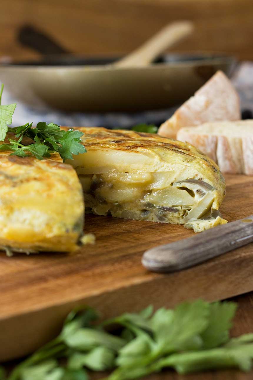 A Spanish omelette on a wooden board with a slice cut out of it