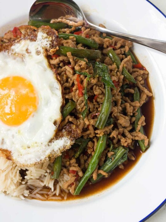 A Thai basil stir-fry from above on a white plate with an egg on top and a spoon on the plate