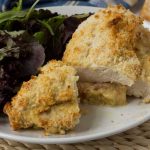 A crispy cheese and ham stuffed chicken breast on a white plate with salad.