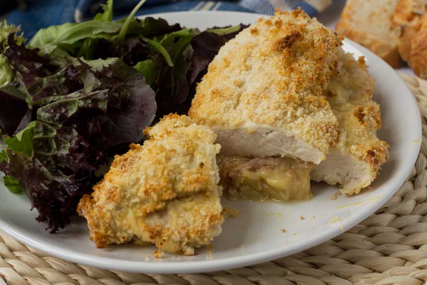 A crispy cheese and ham stuffed chicken breast on a white plate with salad.