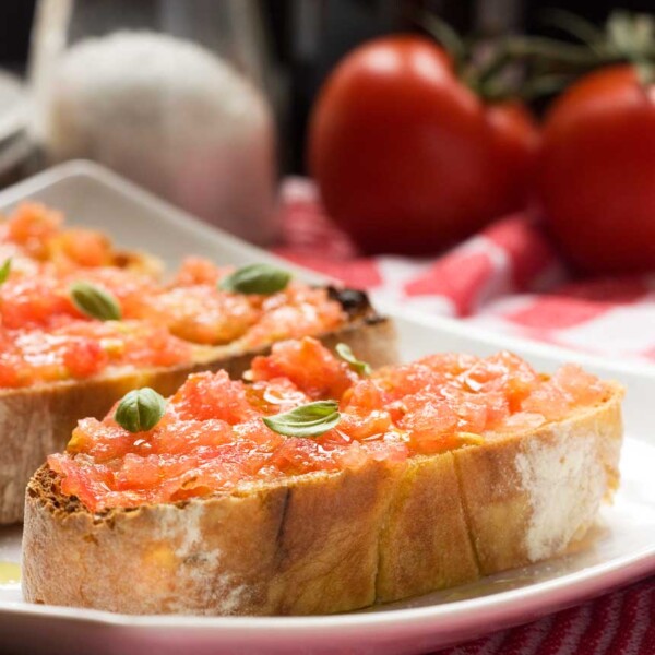 Spanish bruschetta (pan con tomate) close up on a white plate with ingredients behind