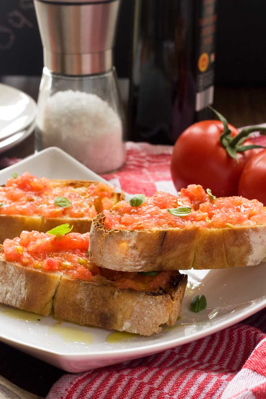 Tomato bruchetta piled onto a plate with ingredients in the background.