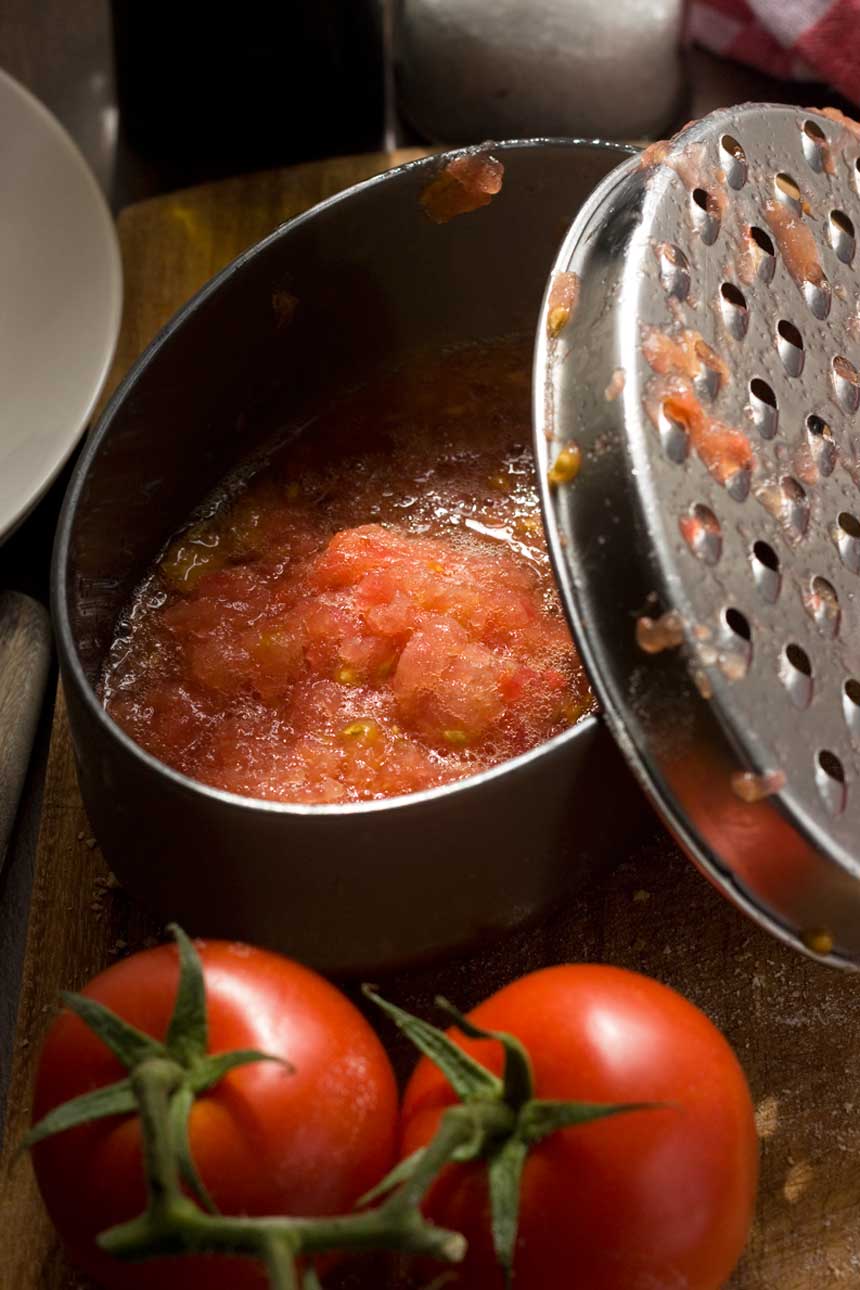 Grated tomato for pan con tomate in a container with tomatoes in the foreground.