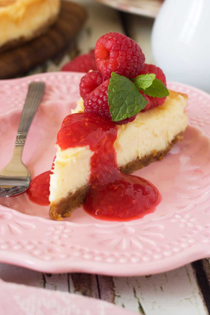 closeup of a piece of White chocolate baked cheesecake with raspberry coulis on a pink plate and with a fork