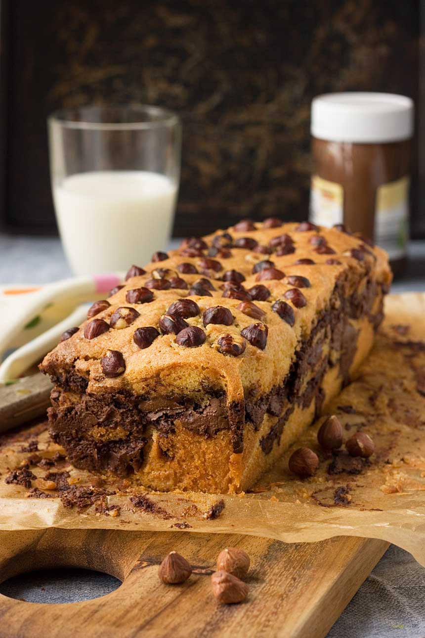 A Nutella swirl loaf on a piece of brown baking paper and with a glass of milk and a jar of Nutella in the background