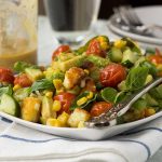 A square plate of crispy halloumi salad with tomato, corn and avocado on a white and blue tea towel