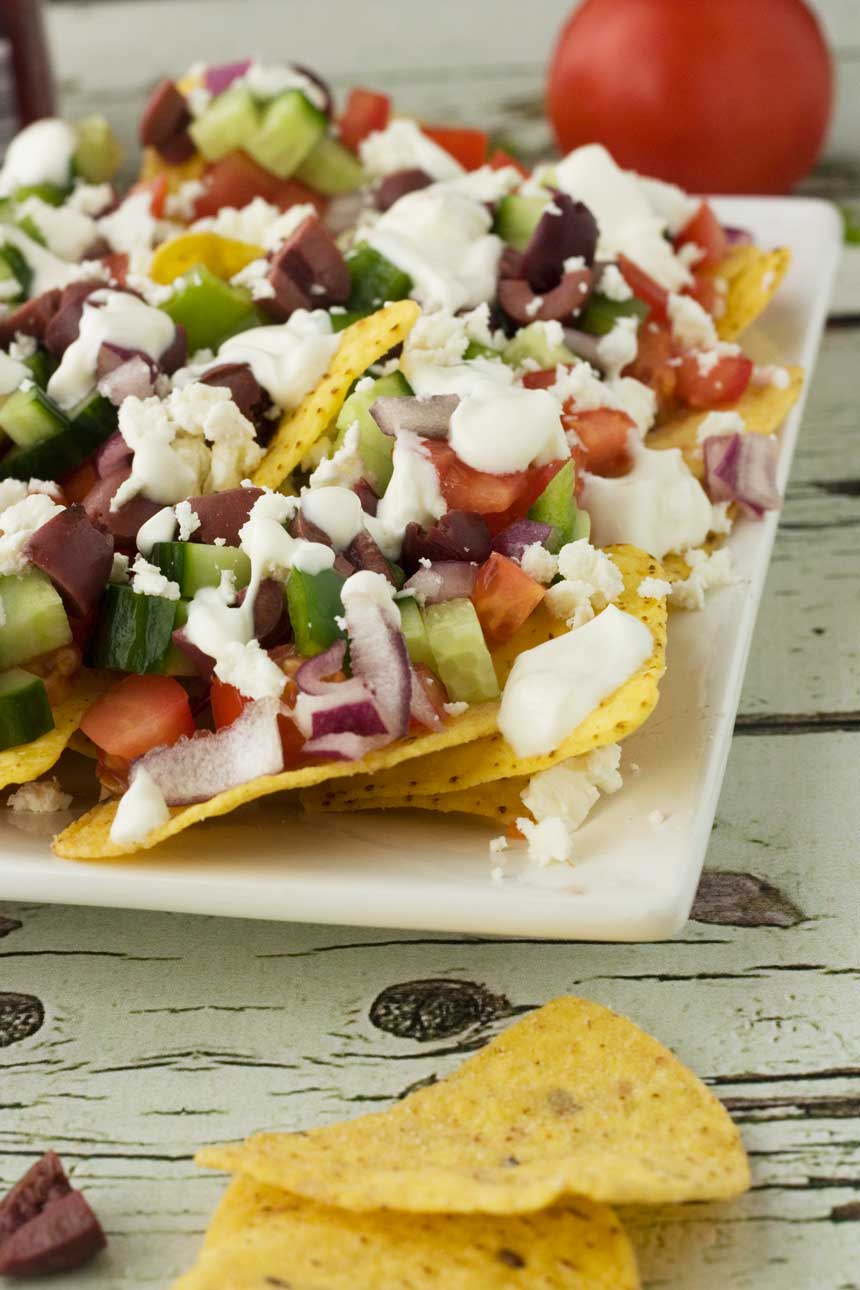 Closeup of the corner of a plate of Greek nachos on a white wooden background.