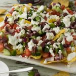 Closeup of Greek nachos on a white square plate.