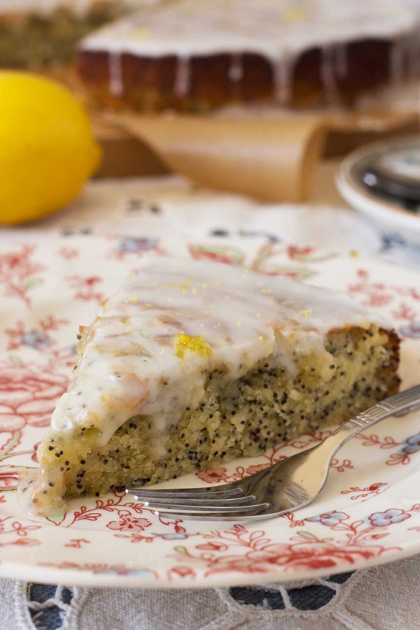 A piece of lemon poppy seed drizzle cake on a pink patterned plate with a fork.