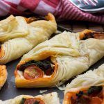 Chorizo and puff pastry tarts in a row on a baking tray with a red tea towel behind.