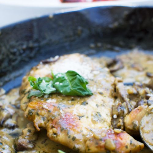 Close up of creamy pesto chicken with parmesan and mushrooms in a cast iron pan