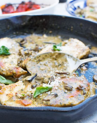 a close up of some creamy pesto chicken in a cast iron skillet with a serving spoon