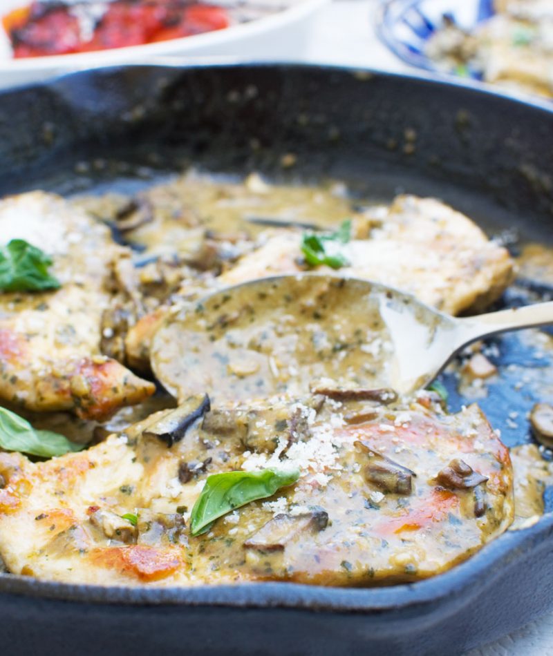 a close up of some creamy pesto chicken in a cast iron skillet with a serving spoon