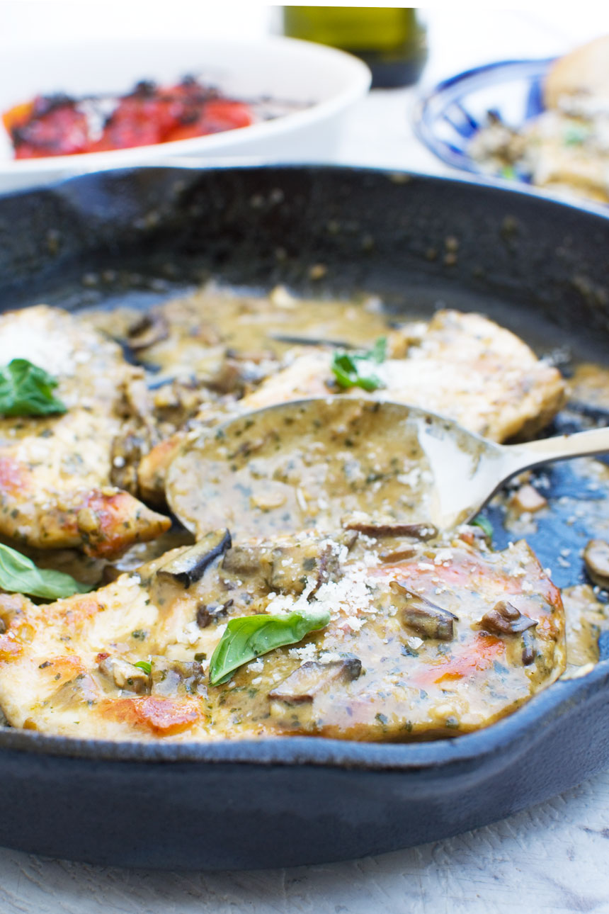 a close up of some creamy pesto chicken in a cast iron skillet with a serving spoon